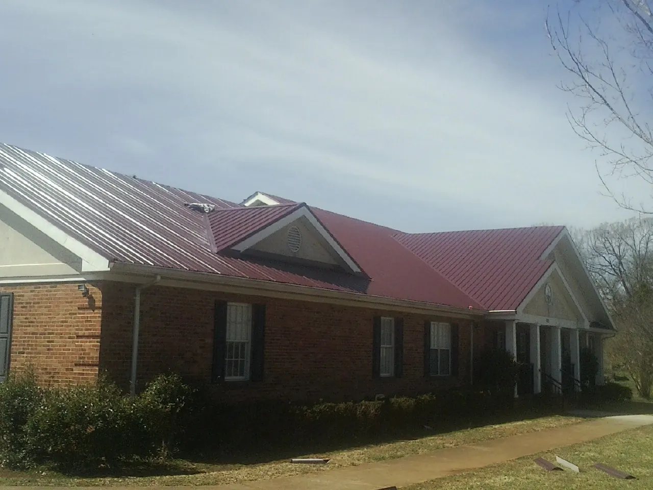 Red metal roof with gabled entries on a long brick building, from a Hail Damage Roof Repair job in Blue Ridge