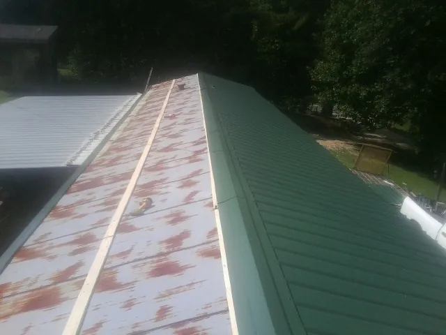 Old rusted panels beside newly installed green metal roofing — Wind Damage Roof Repair by Roofing Brothers in Blue Ridge