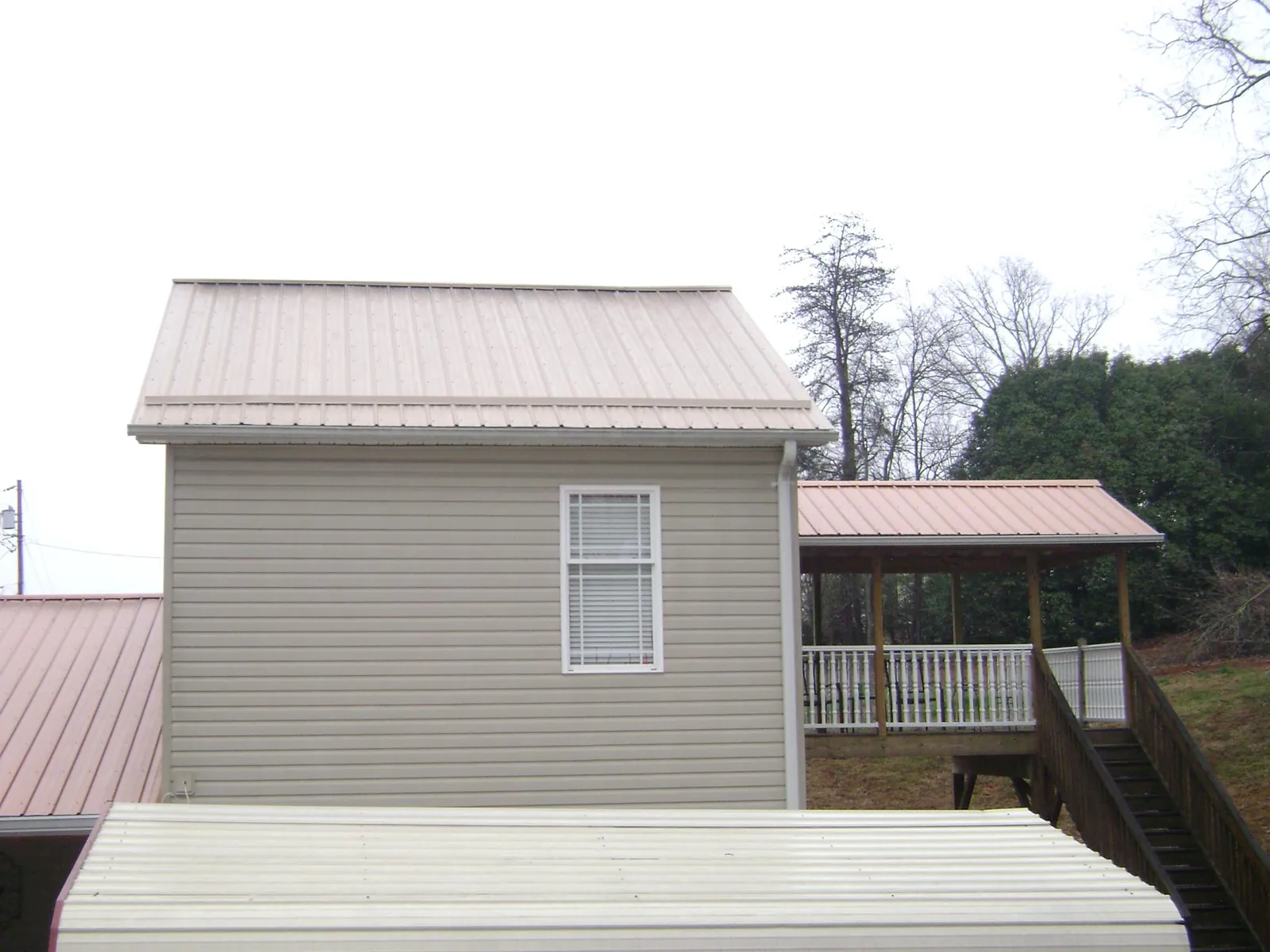 Tan metal roofs on a two story addition and attached porch, from a Roof Replacement job in Blue Ridge